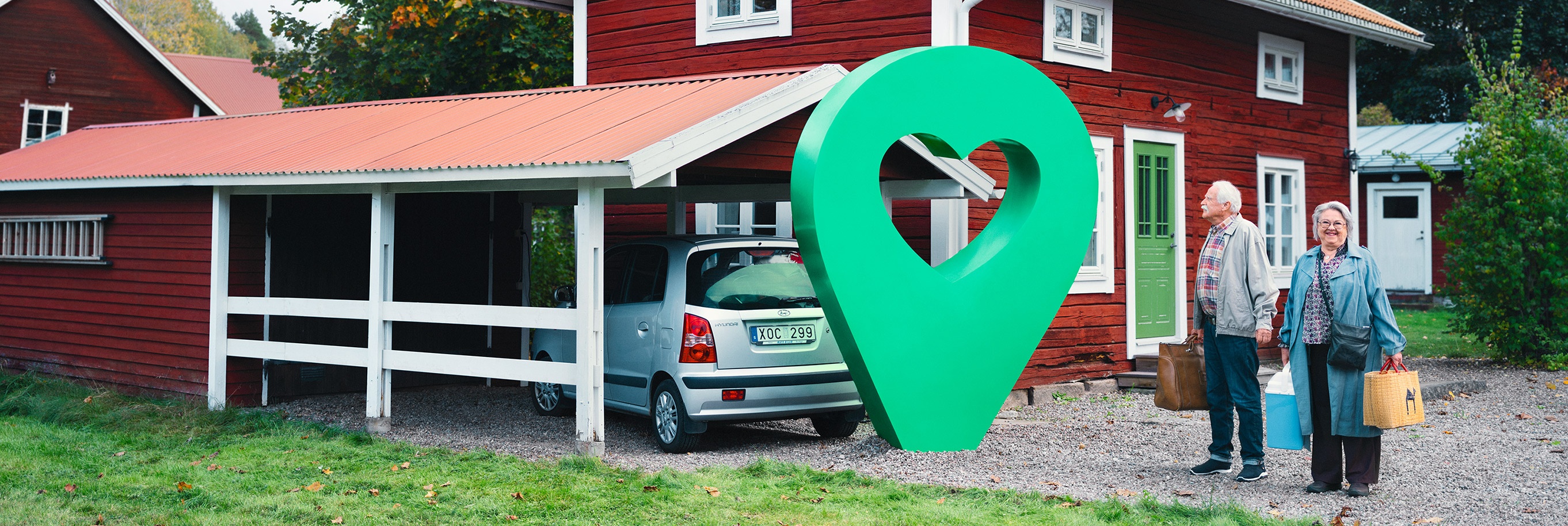 Ett rött sommarhus med carport och två glada personer. En grön pin med hjärta är placerad vid huset.