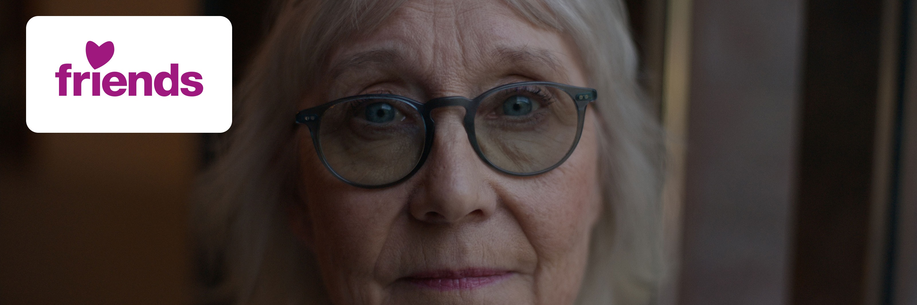 Äldre person med glasögon tittar mot kameran bredvid Friends-logotypen.