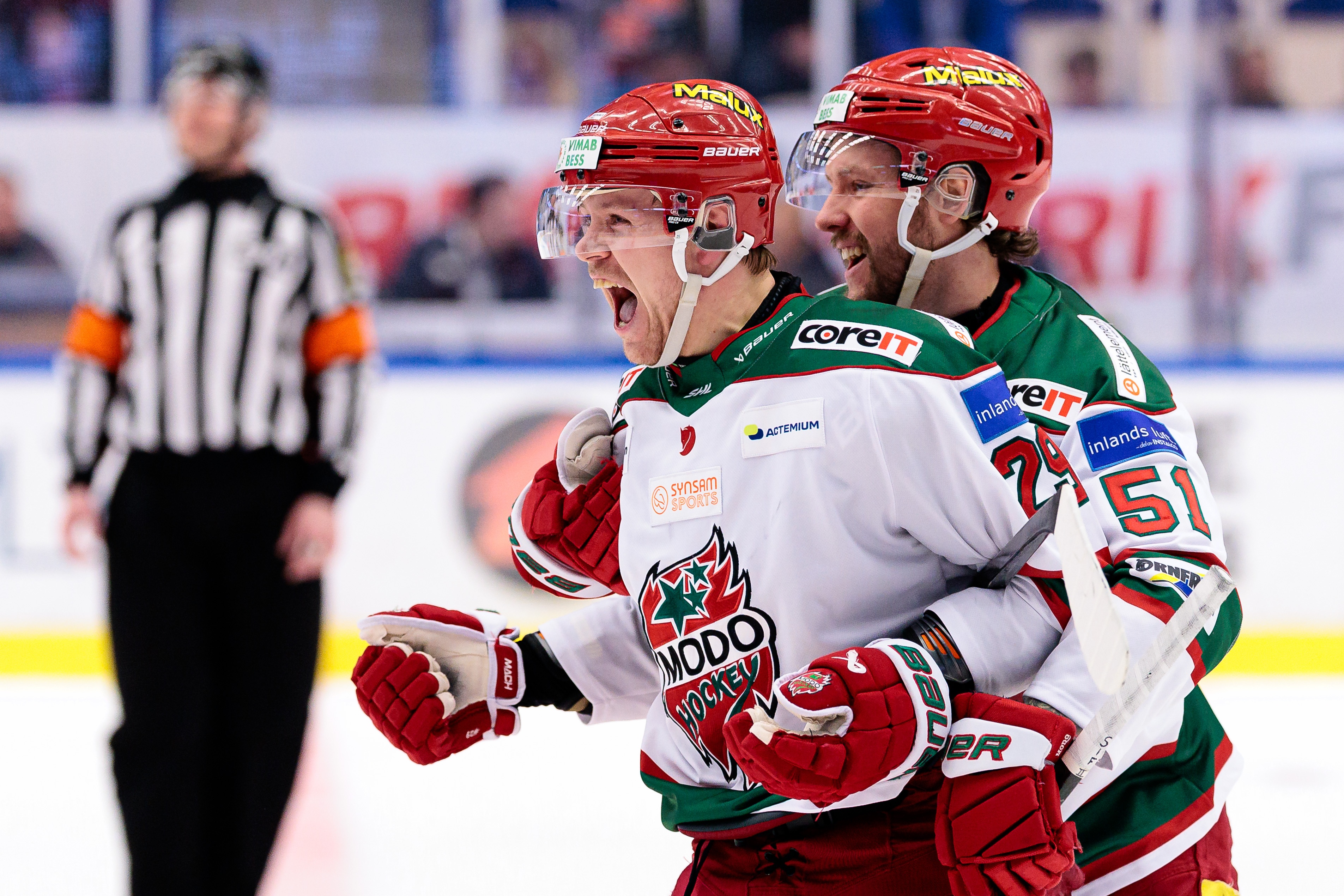 Två Modo-hockeyspelare, inklusive Mikkel Aagaard, på isen under en match. Spelare i grönt och rött.