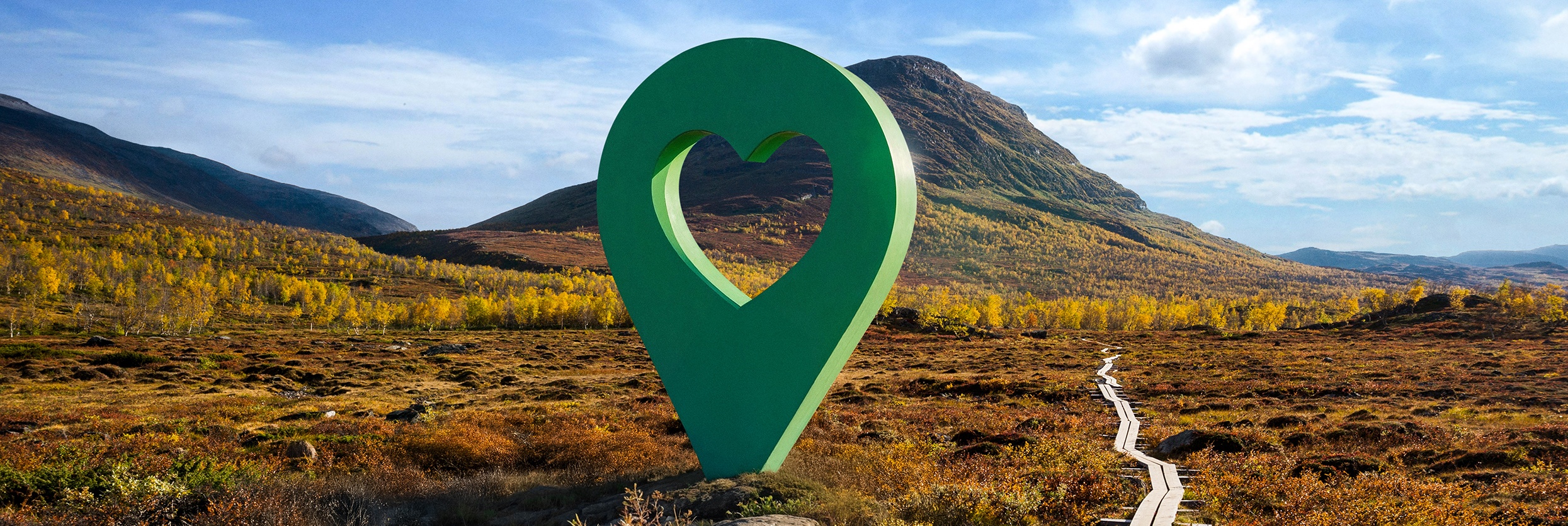 Bild av Lyckplatsen med en stor grön hjärtformad platsmarkering i ett vackert landskap under blå himmel.