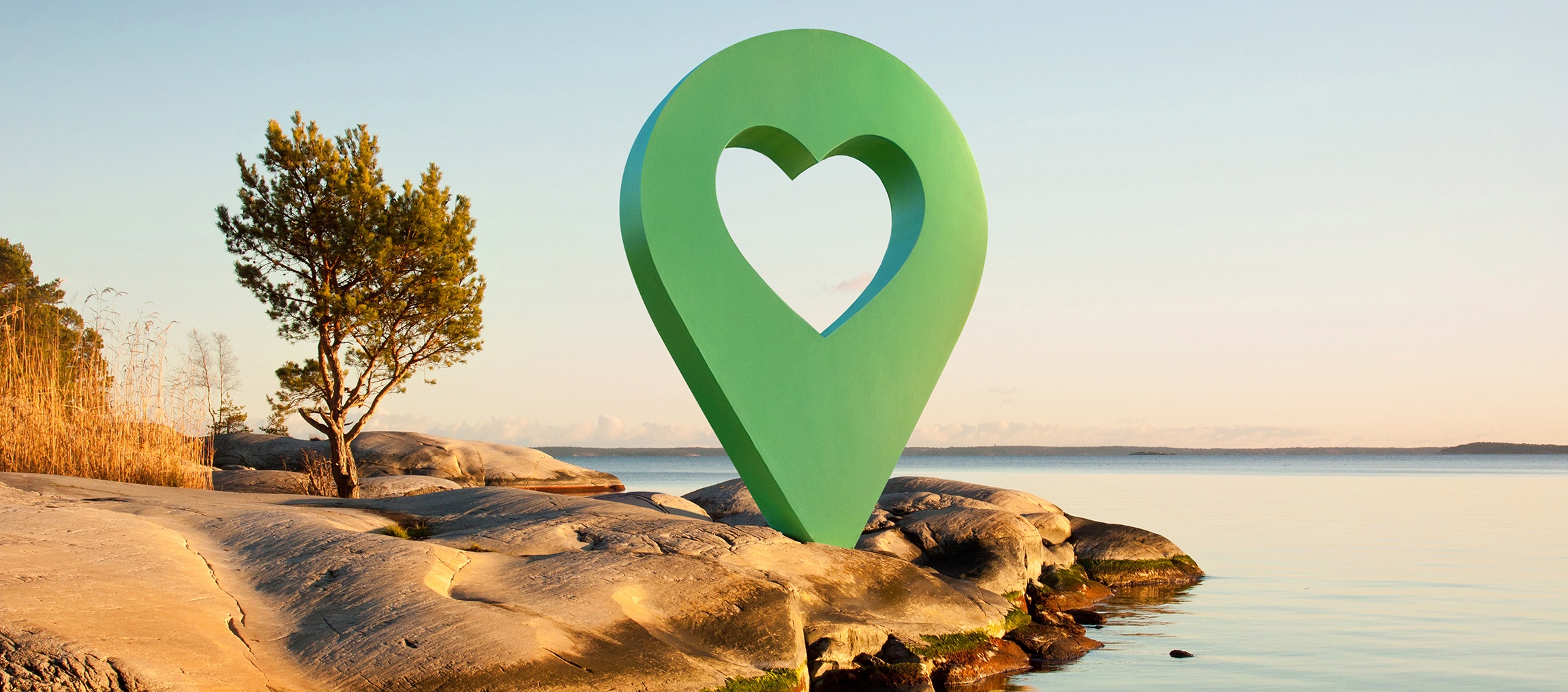 En ikon med hjärta mitt i på en klippa vid havet med en soluppgång och ett ensamt träd till vänster.