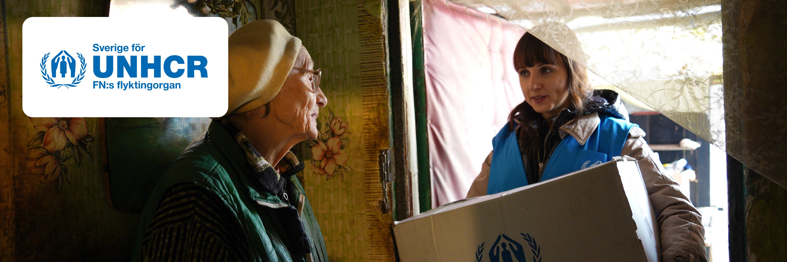 UNHCR-anställd som levererar en låda till en äldre person i Ukraina, med logga i hörnet.