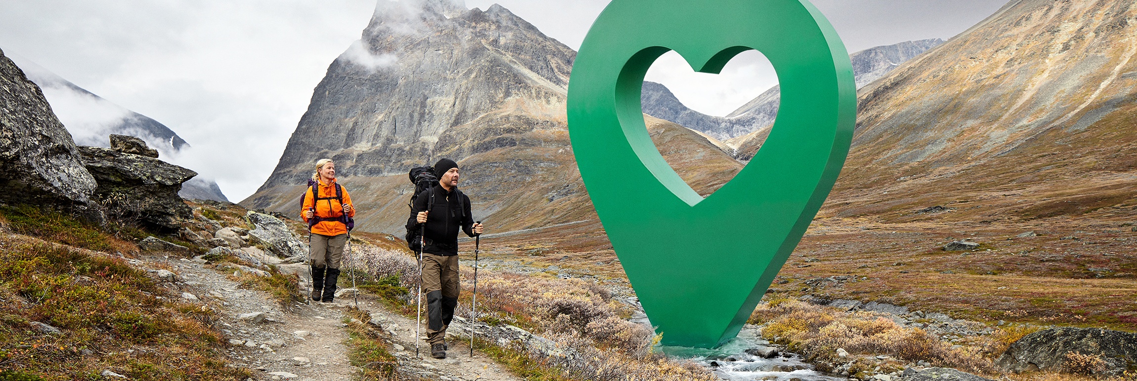 Två vandrare på en fjällstig i Sverige närmar sig en stor grön markör med hjärta, symboliserar Lyckplatsen.