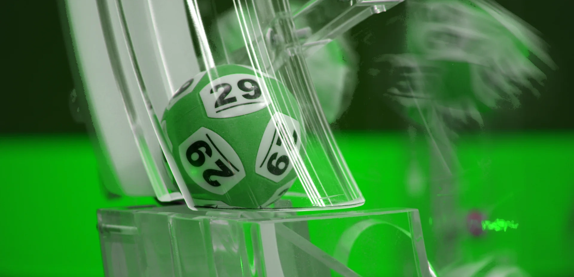 Grön lottoboll i en dragning med nummer 29 synlig i en lottotrumma med grön bakgrund.
